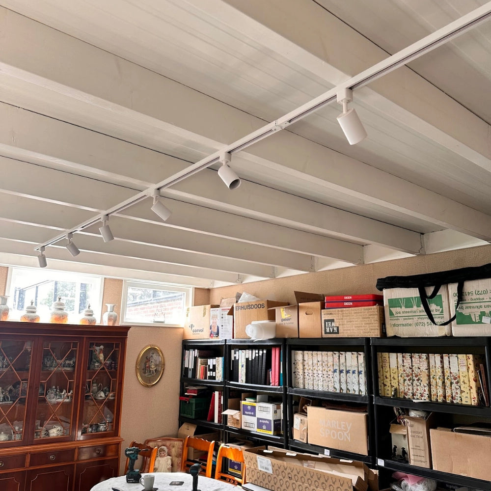 Witte railverlichting aan het plafond met meerdere spots en hangende lampen.